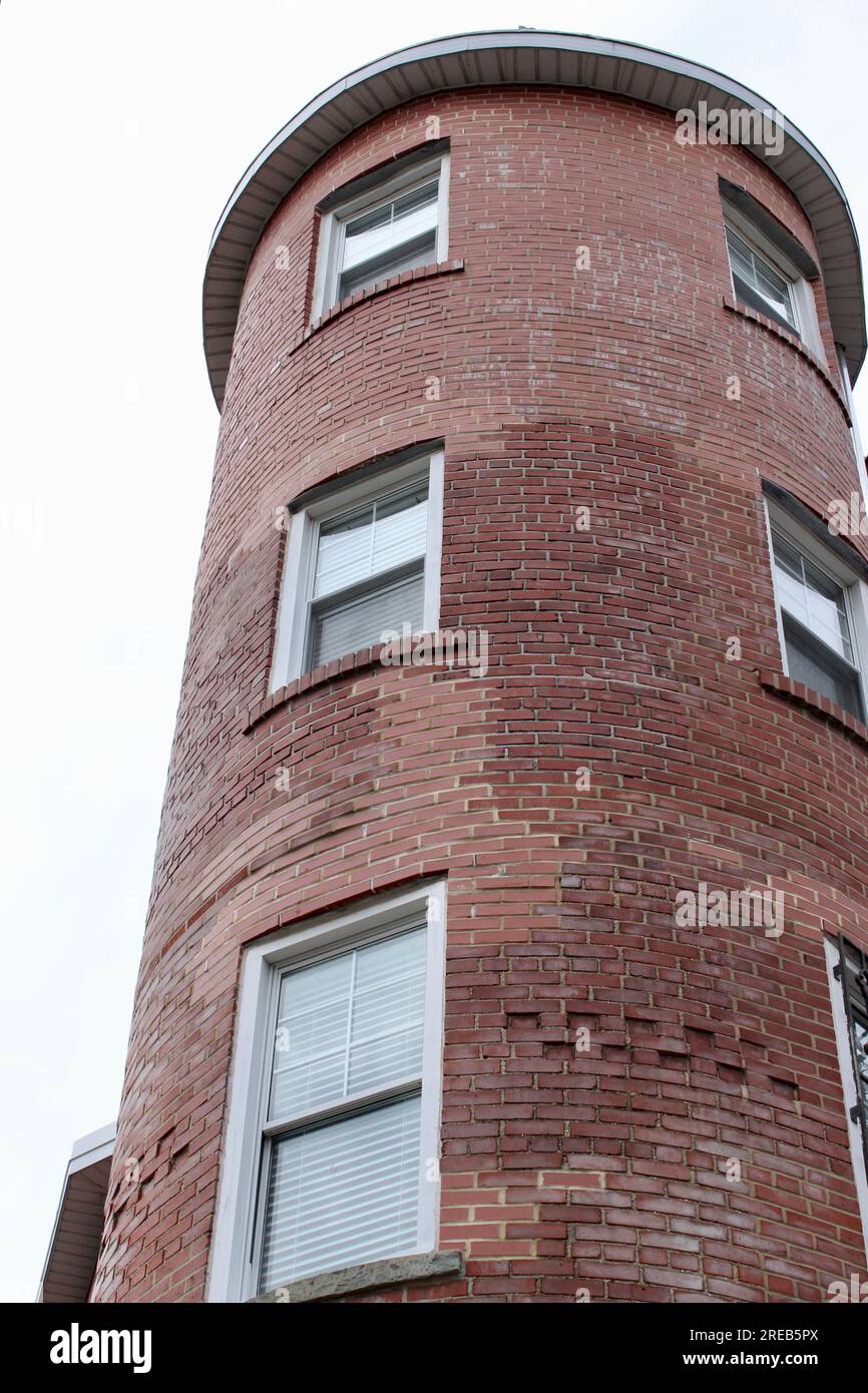 Vista ad angolo basso di una torre curva in mattoni rossi su un edificio storico residenziale o commerciale, con file di finestre con cornice bianca su una overcas Foto Stock