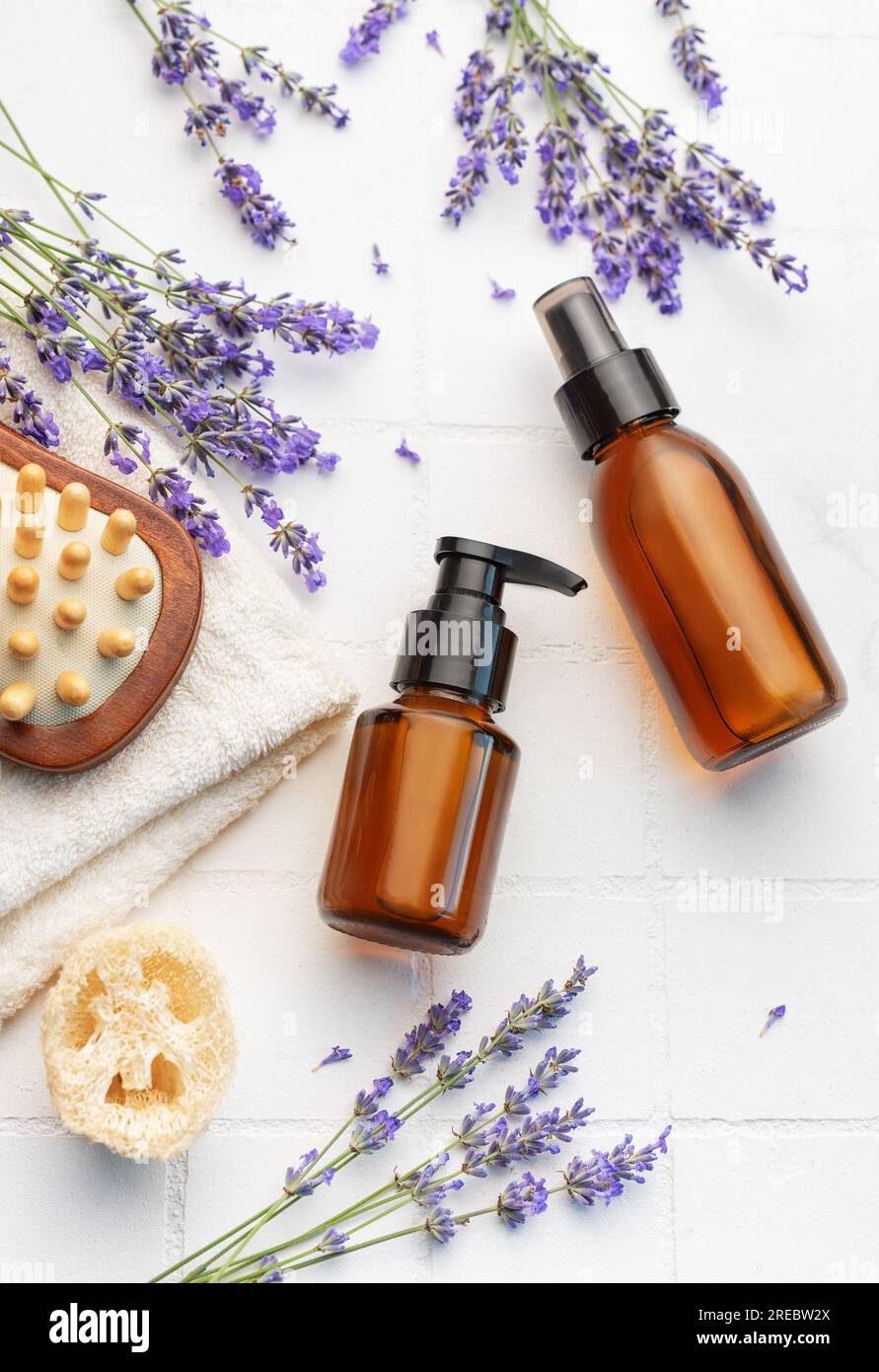 Vasca idromassaggio con lavanda. Sale di lavanda, olio essenziale naturale, spazzole per massaggi e lavanda fresca su fondo di piastrelle bianche. Foto Stock