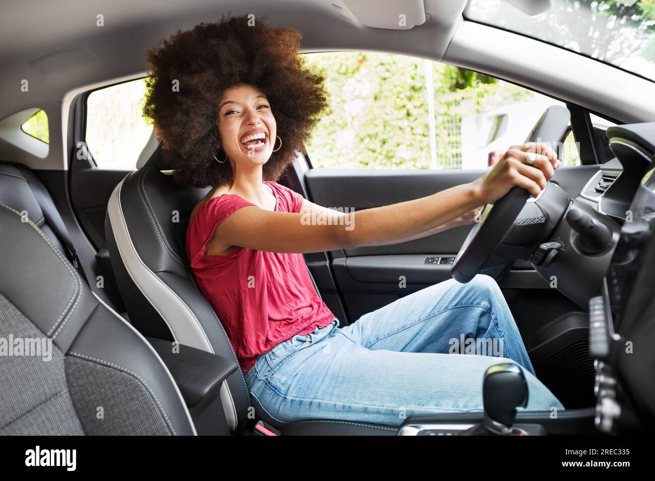 Vista laterale della giovane donna afroamericana in abiti casual con acconciature afro sedute e ridendo in auto guardando la macchina fotografica Foto Stock
