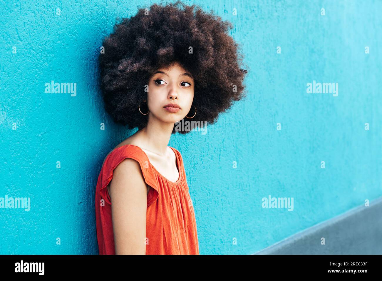 Ritratto laterale di una giovane donna marocchina in tessuto casual con acconciatura afro che guarda la fotocamera mentre si trova in piedi su sfondo blu Foto Stock