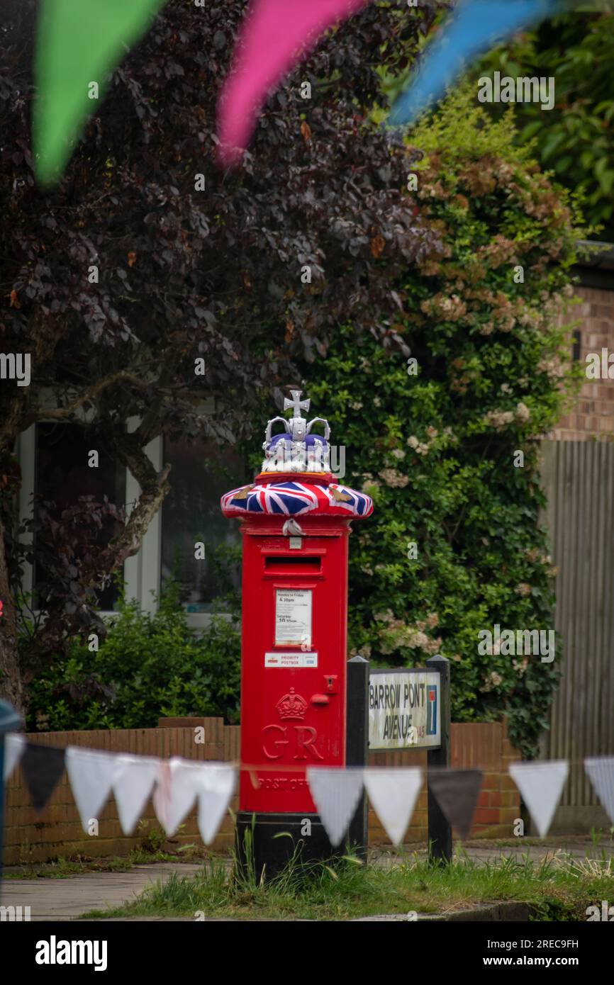 Copricartolina in maglia su una cassetta delle lettere rossa che si erge fiero del bordo dello streetparty e indossa una corona. Foto Stock