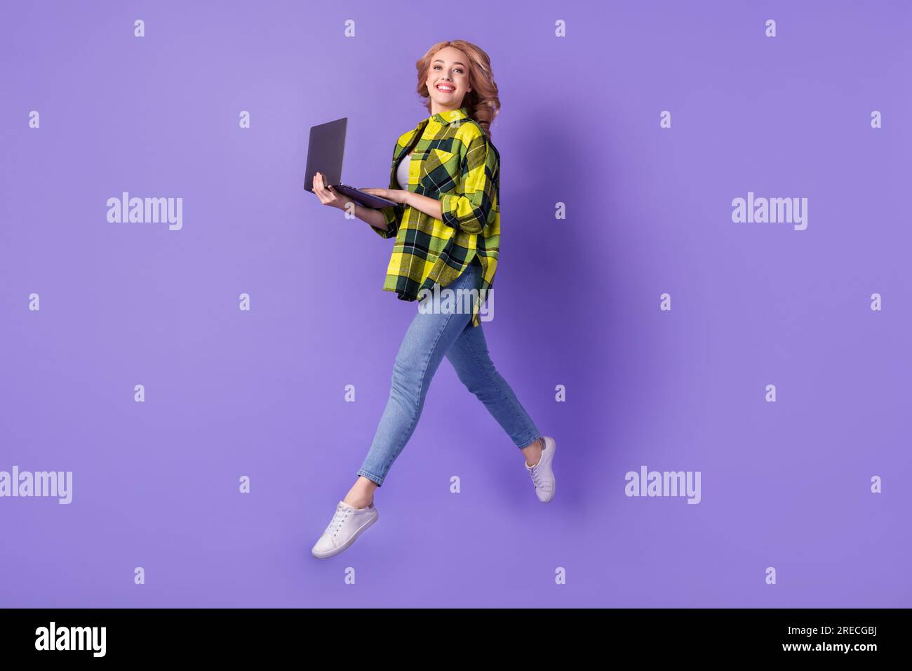 Foto di una ragazza che corre con un computer portatile comodo dispositivo per studiare mentre è isolata su uno sfondo di colore viola Foto Stock