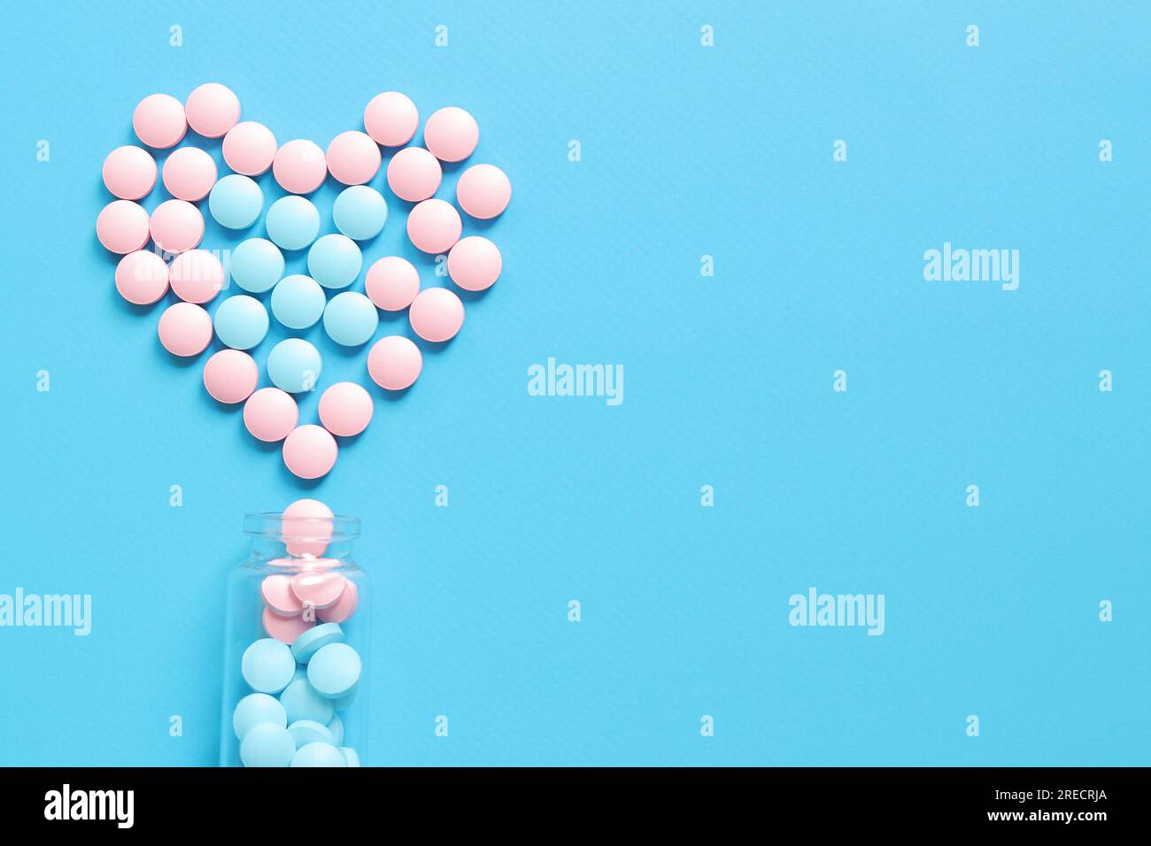 Bottiglia di vetro con pillole rosa e blu. Cuore rivestito di vitamine su sfondo blu, vista dall'alto. Sanità, pillole mediche e integratori alimentari. PH Foto Stock