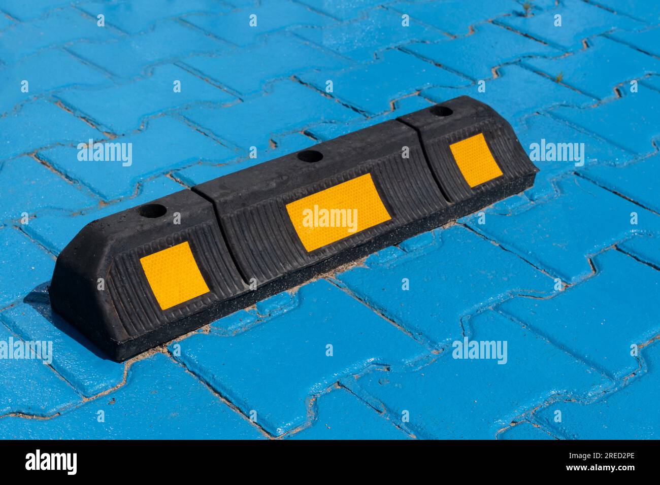 Una vista ravvicinata di un singolo fermo di parcheggio in gomma in un parcheggio, che illustra il concetto di sicurezza del parcheggio. Foto Stock