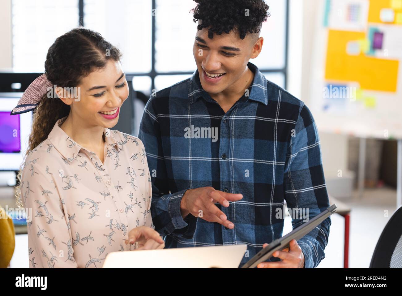 Uomo e donna soddisfatti e diversificati con un tablet digitale e un notebook che discutono in ufficio Foto Stock