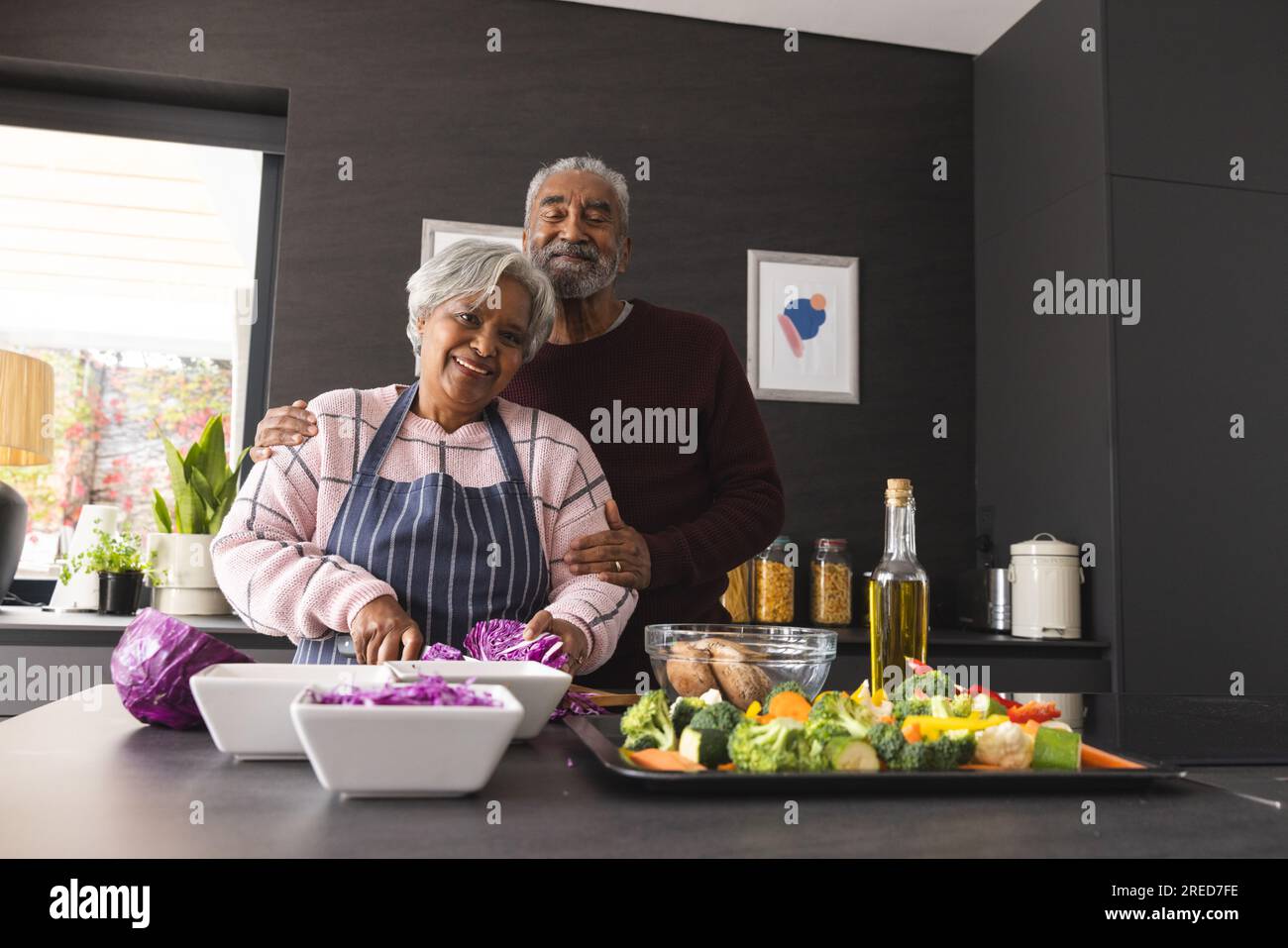 Ritratto di una felice coppia birazziale anziana che prepara verdure e abbraccia in cucina a casa Foto Stock