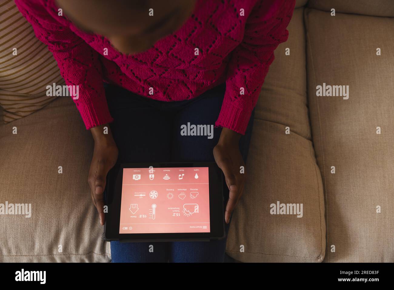 Donna afroamericana sul divano che usa un tablet con interfaccia domestica intelligente sullo schermo a casa Foto Stock