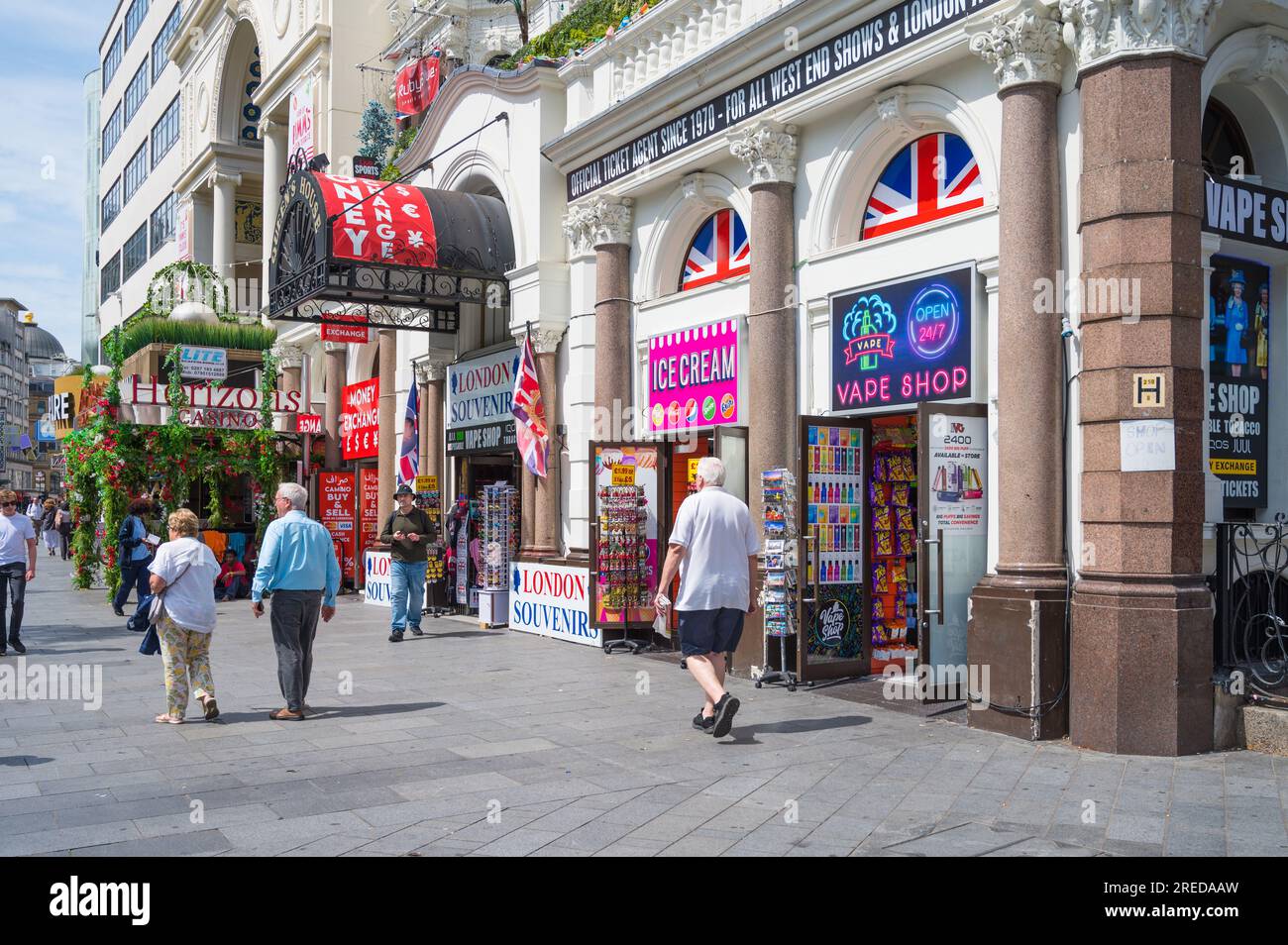 Le persone che camminano in Leicester Square in una soleggiata giornata estiva passano accanto ai colorati negozi adiacenti al cinema IMAX e all'Empire Casino. Londra, Inghilterra, Regno Unito Foto Stock