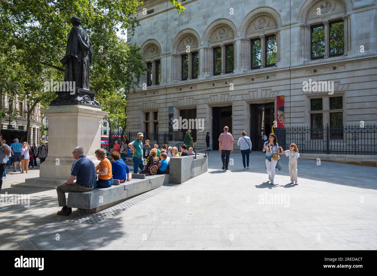 Persone che si rilassano e socializzano sedute su una panchina di pietra in una soleggiata giornata estiva fuori dall'ingresso della National Portrait Gallery. Londra, Inghilterra, Regno Unito Foto Stock