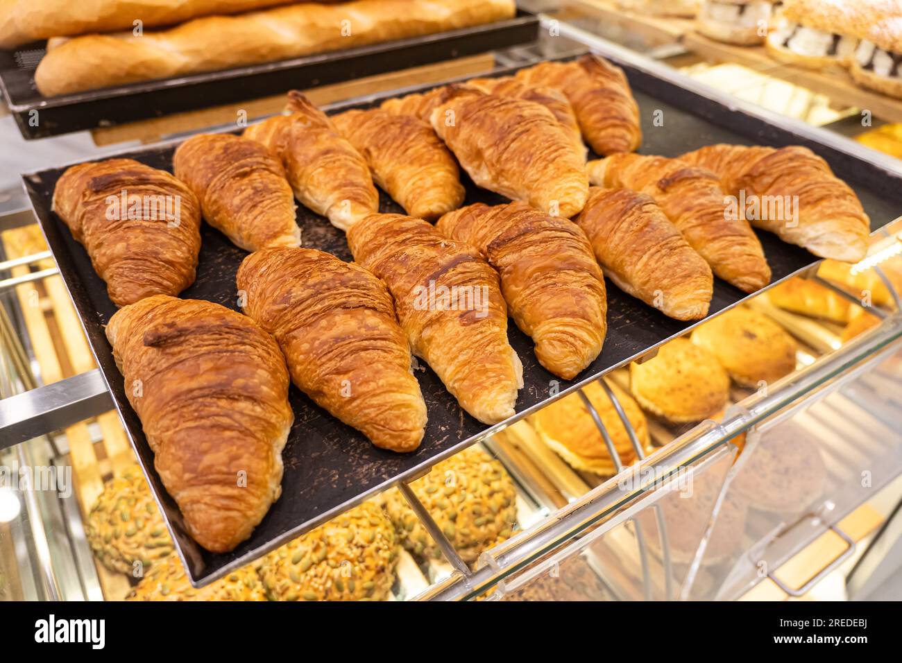 Pasticceria fresca al banco del negozio. Croissant cotti al forno su teglia da forno con carta pergamena. Bagel dolci cotti nel forno caldo. processo di maki Foto Stock