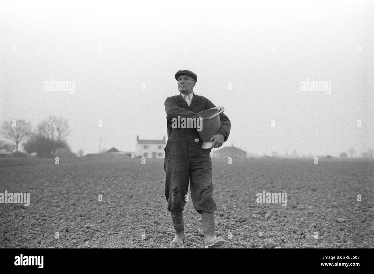 Agricoltore che semina a mano i semi. Walter Howling di Sandygate Lane nella sua toppa alle ginocchia, seminando a mano i semi da un secchio di plastica. Terrington St. Clement, Norfolk, East Anglia, Inghilterra 1974. ANNI '1970 UK HOMER SYKES.. Foto Stock