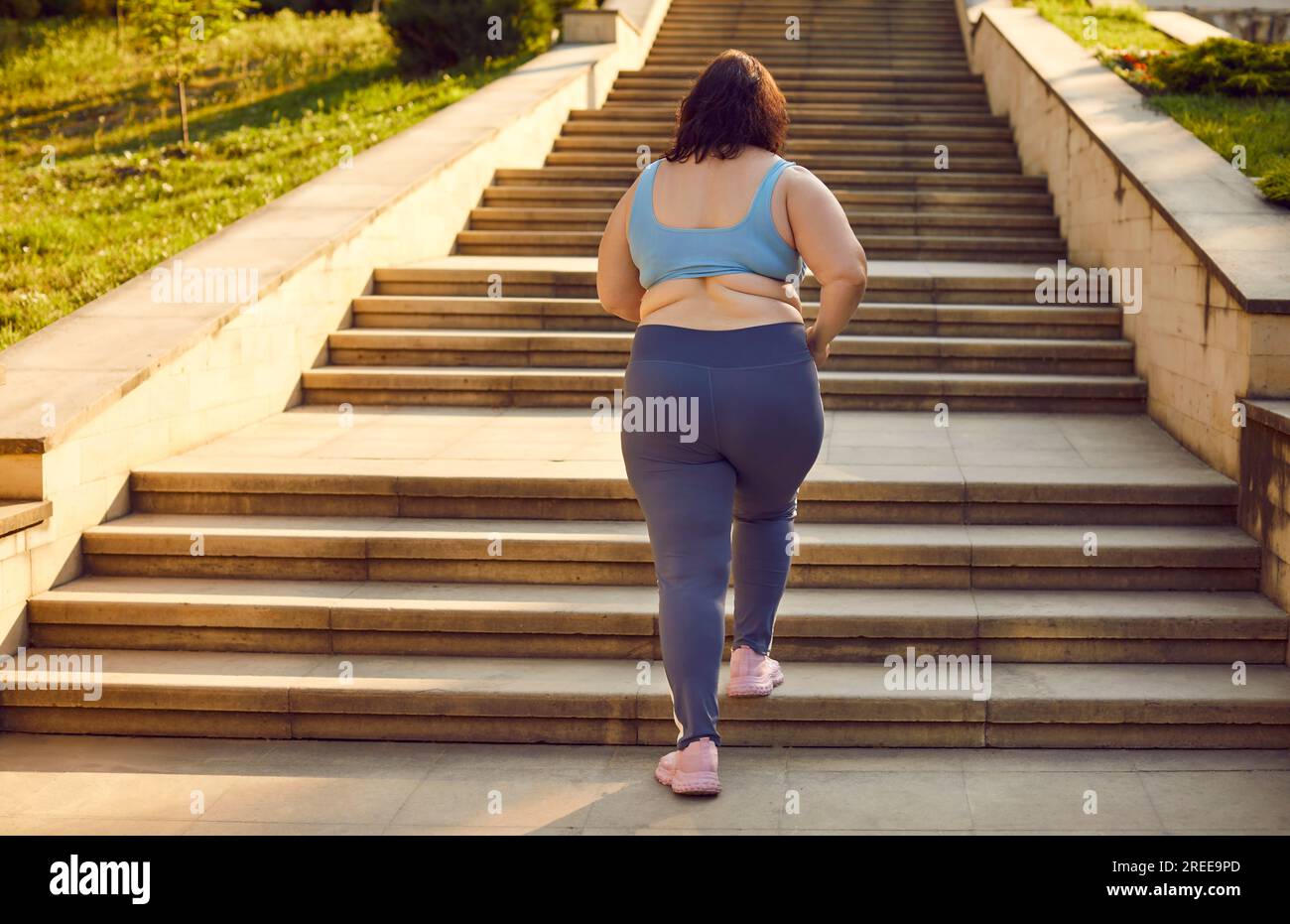 Donna grassa e sorridente in sovrappeso che corre sulle scale del parco estivo della città. Foto Stock