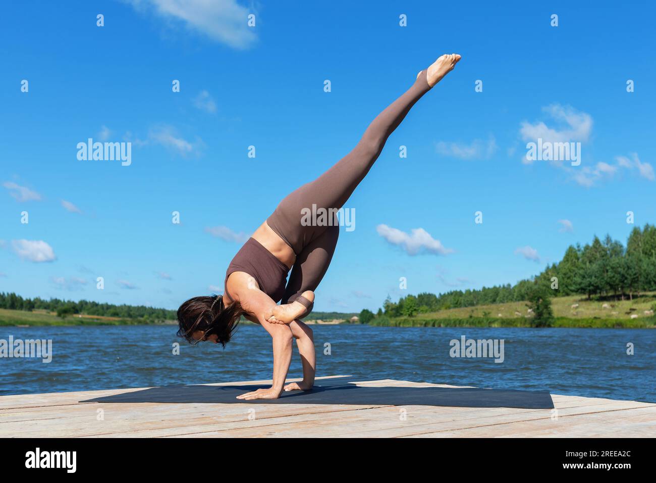 Donna che fa esercizio Eka Pada Bakasana, posa gru con gamba allungata, asana bilanciata, cavalletto a tutta lunghezza, pratica yoga con abbigliamento sportivo lakesi Foto Stock