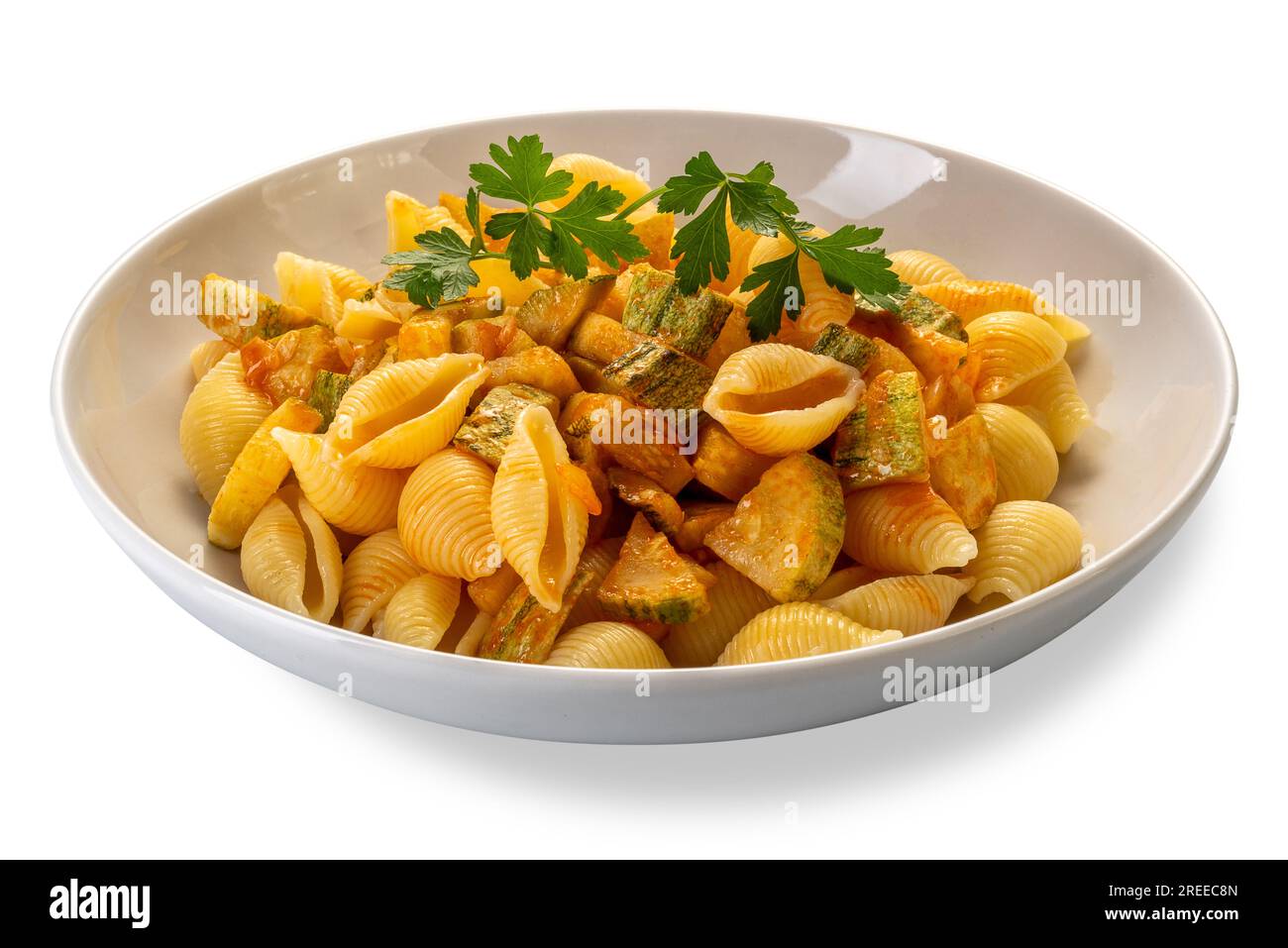 Conchiglie rigate pasta. Maccheroni a forma di conchiglia rigata con zucchine e salsa di pomodoro con foglie di prezzemolo in piatto bianco isolato su bianco con cl Foto Stock