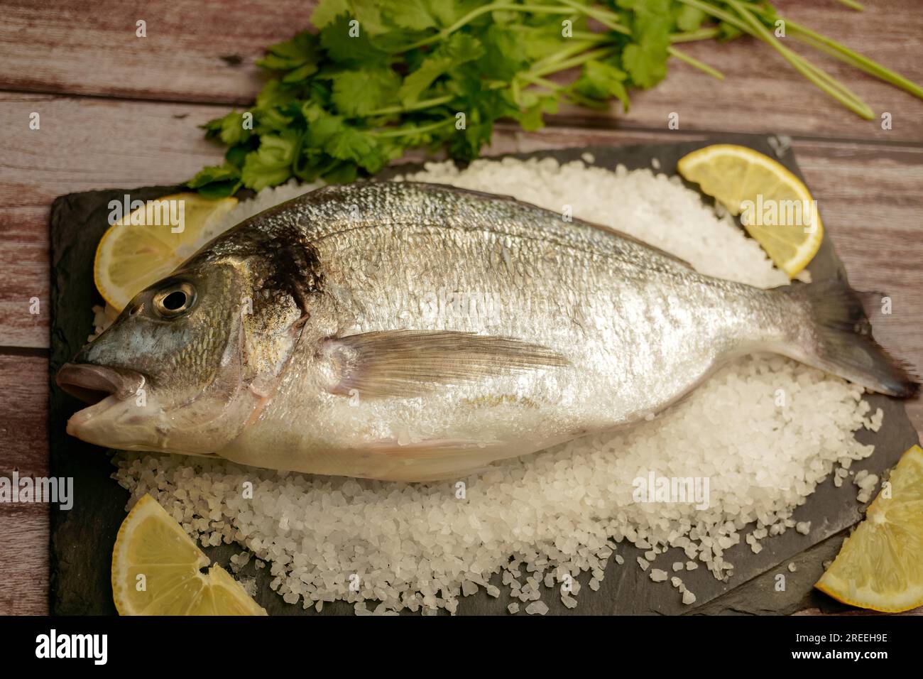 Orata di mare fresca su un'ardesia con sale e limone su un tavolo di legno con uno spazio copia Foto Stock