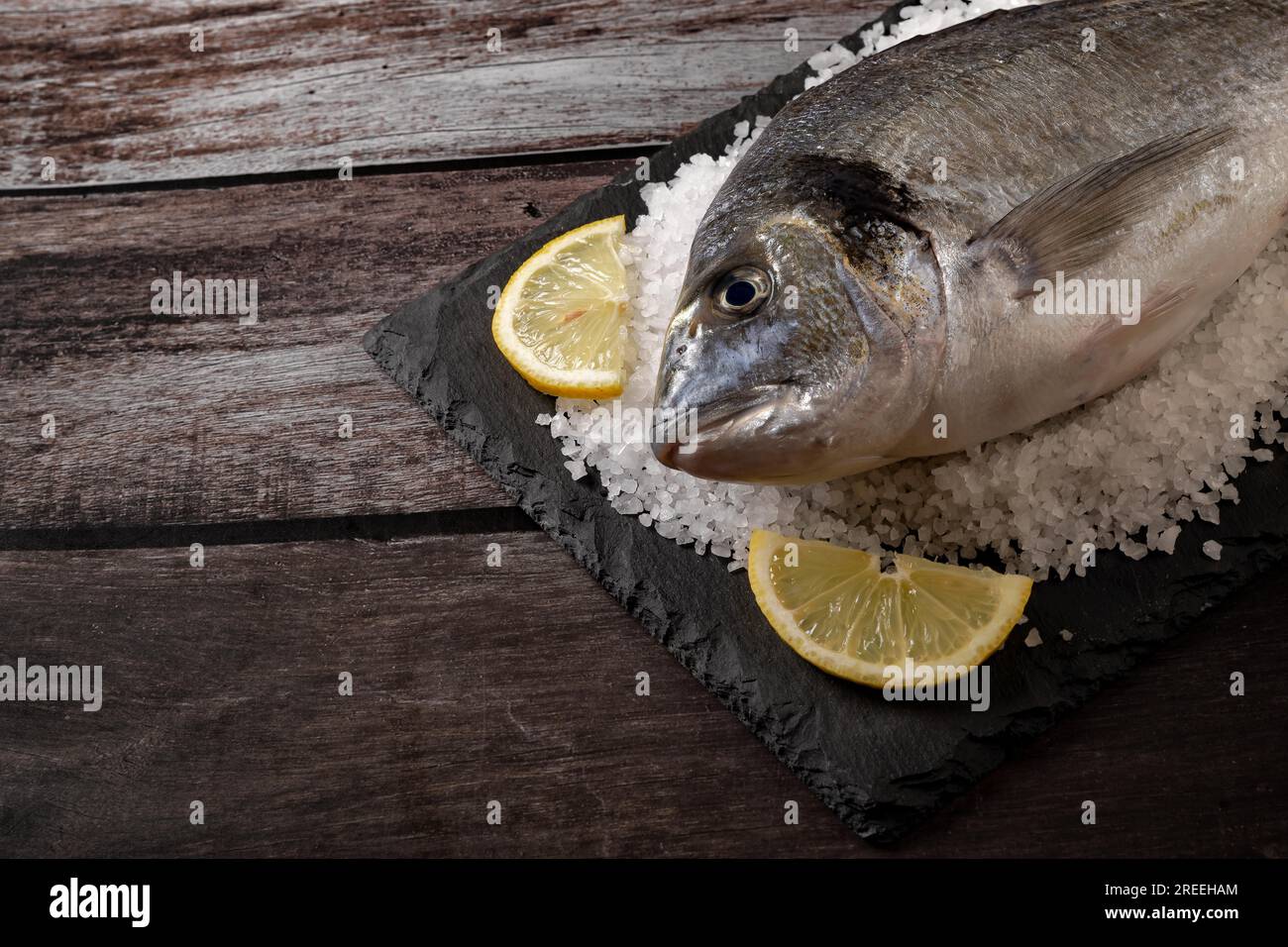 Orata di mare fresca su un'ardesia con sale e limone su un tavolo di legno con uno spazio copia Foto Stock