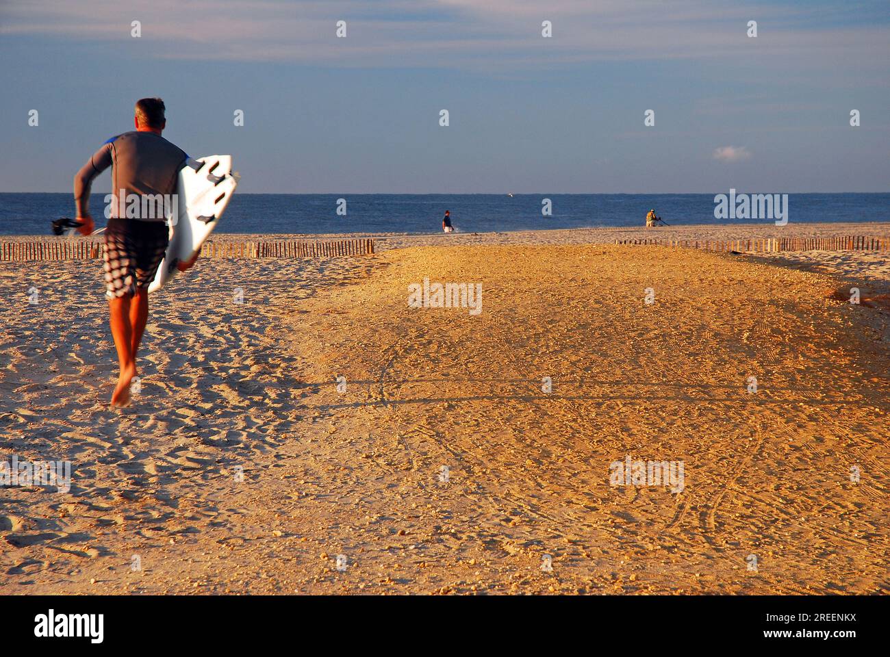 Un uomo adulto porta la sua tavola per una giornata di surf lungo la riva Foto Stock
