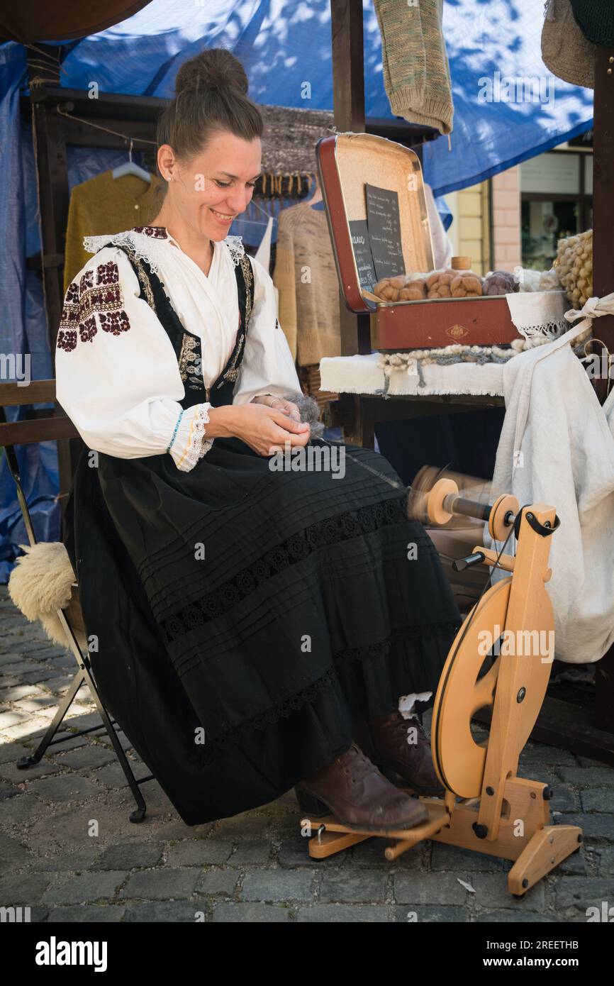KEZMAROK, SLOVACCHIA - JUL 9, 2023: Artigiana che utilizza la ruota rotante per trasformare la lana in filato all'European Folk and Crafts Festival di Kezmarok, in slovacco Foto Stock