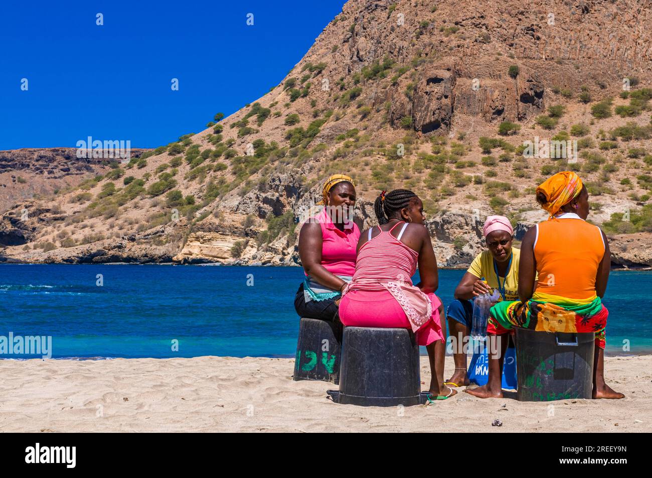 Donne dalla pelle scura, sedute a spiaggia di sabbia e che parlano tra loro. Tarrafal. Santiago. Cabo Verde. Africa Foto Stock