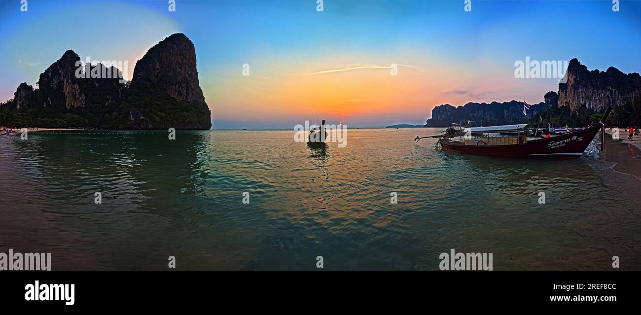 Foto panoramica del tramonto a Railay Beach a Krabi in un cielo senza nuvole incorniciato da rocce e con una tipica barca a coda lunga in primo piano fotografato Foto Stock