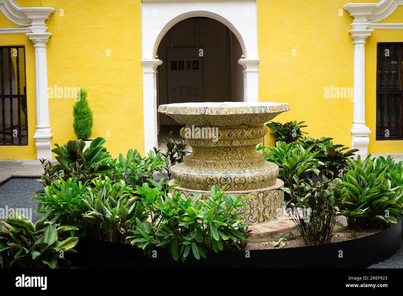 Fontana con schema dettagliato circondata da piante verdi vicino all'edificio giallo Foto Stock