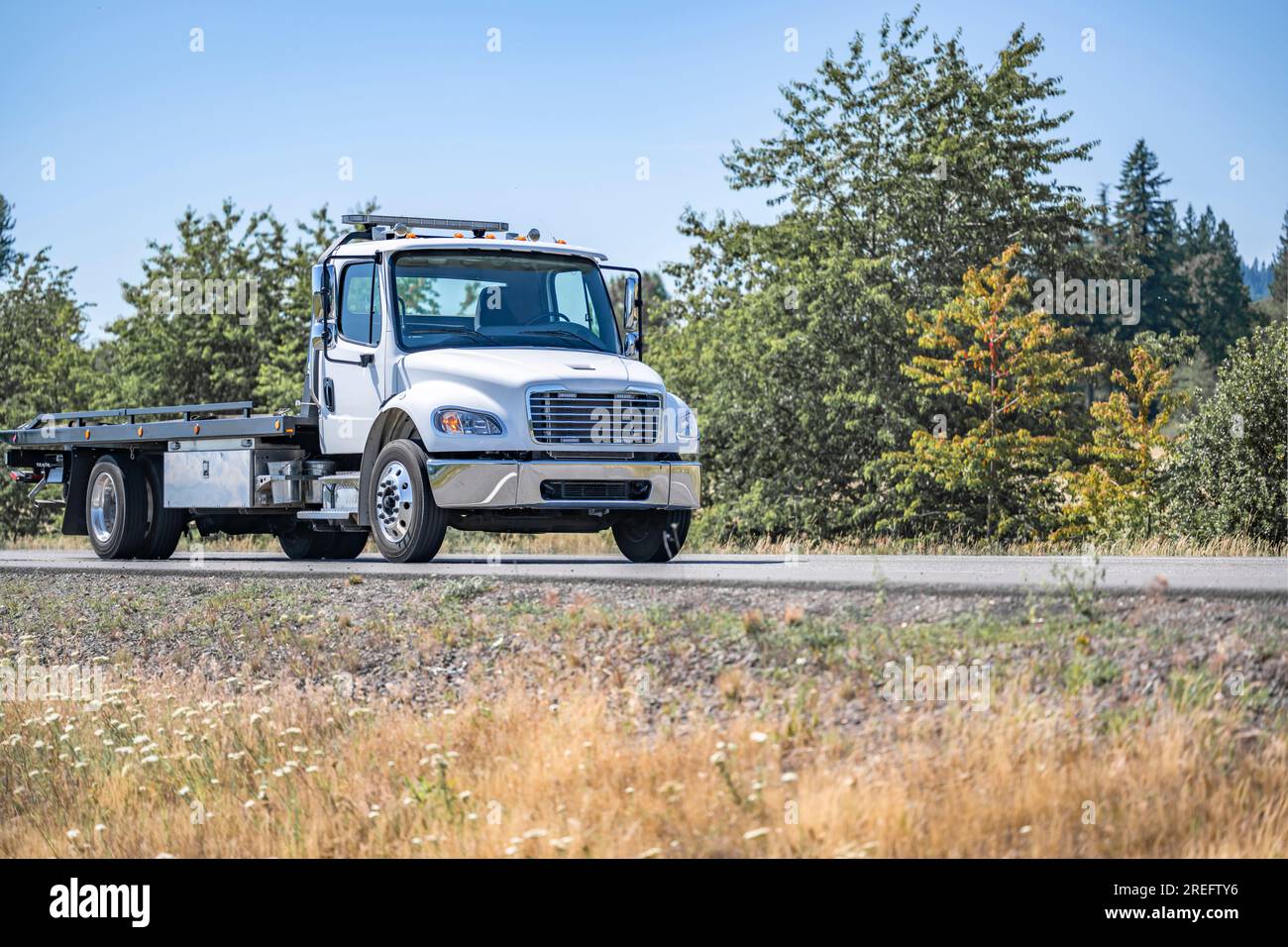 Trattore per semi-carro da lavoro standard per impieghi medi con cabina corta bianca con rimorchio a pianale piatto scorrevole per facilitare le operazioni di carico e scarico del carico Foto Stock