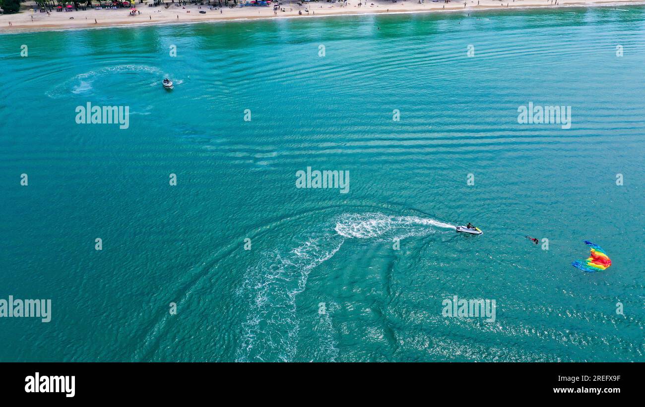 Vista dall'alto delle acque cristalline del mare con il personale e i turisti che si dirigono verso la barca dopo aver finito il paracadutismo ascensionale Foto Stock