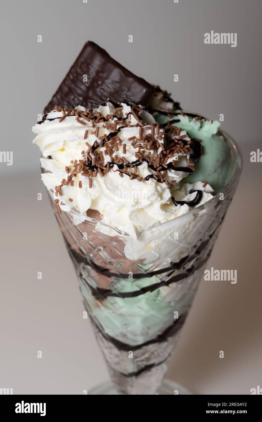 Sundae di gelato alla menta servito in un bicchiere di sundae alto con 3 cucchiai di gelato, oltre a una varietà di salse e condimenti. Foto Stock