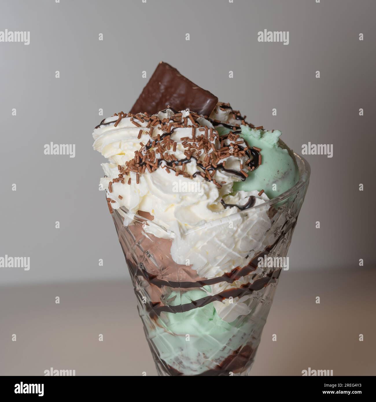 Sundae di gelato alla menta servito in un bicchiere di sundae alto con 3 cucchiai di gelato, oltre a una varietà di salse e condimenti. Foto Stock
