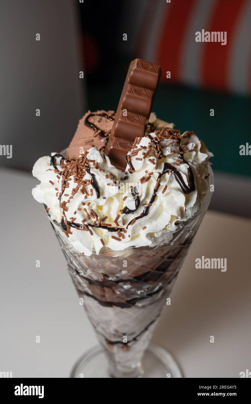 Gelato al cioccolato servito in un bicchiere di sundae alto con 3 cucchiai di gelato, oltre a una varietà di salse e condimenti. Foto Stock