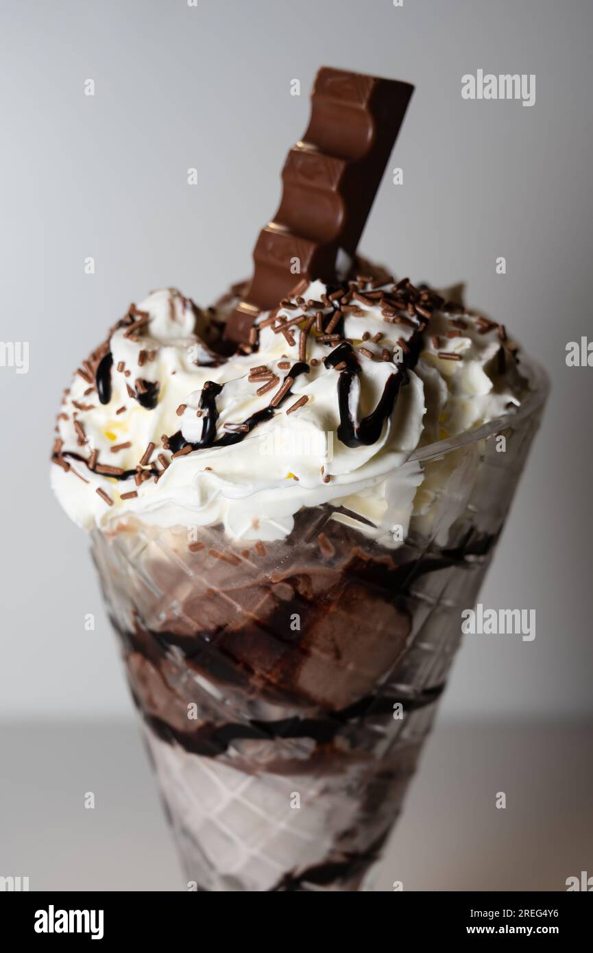 Gelato al cioccolato servito in un bicchiere di sundae alto con 3 cucchiai di gelato, oltre a una varietà di salse e condimenti. Foto Stock