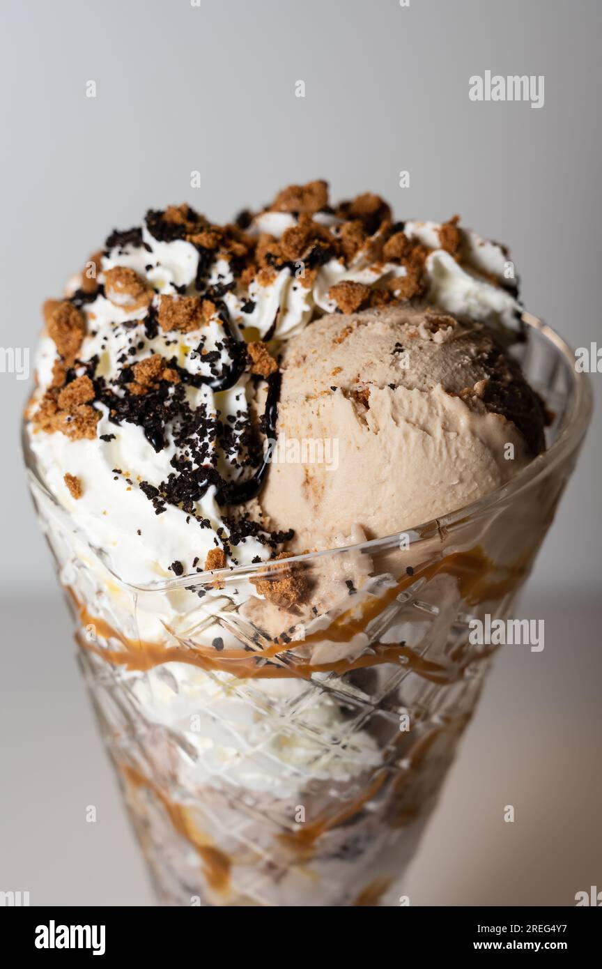 Biscotti Crunch gelato sundae serviti in un alto bicchiere di sundae con 3 cucchiai di gelato, oltre a una varietà di salse e condimenti. Foto Stock