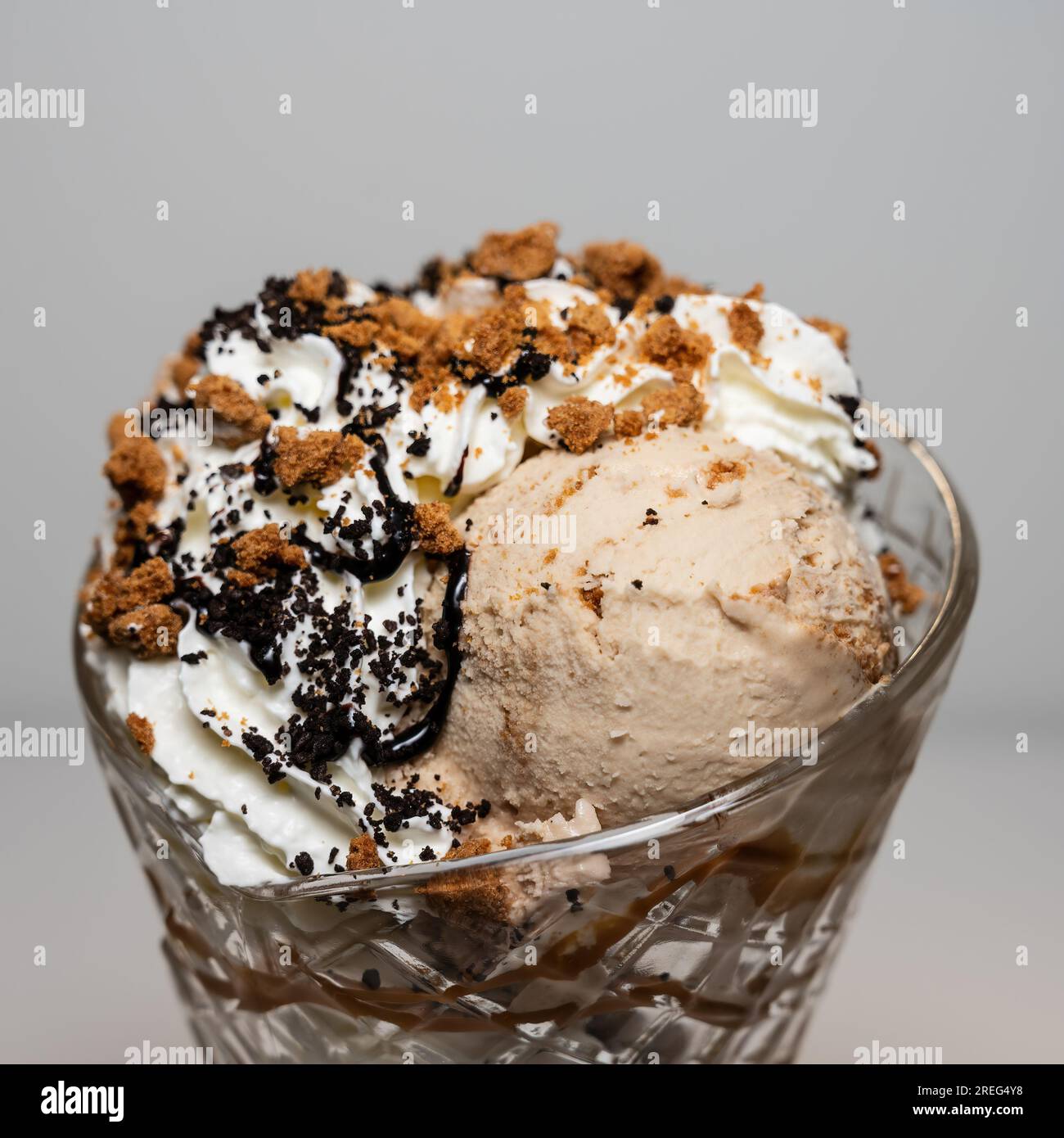 Biscotti Crunch gelato sundae serviti in un alto bicchiere di sundae con 3 cucchiai di gelato e una varietà di condimenti. Foto Stock