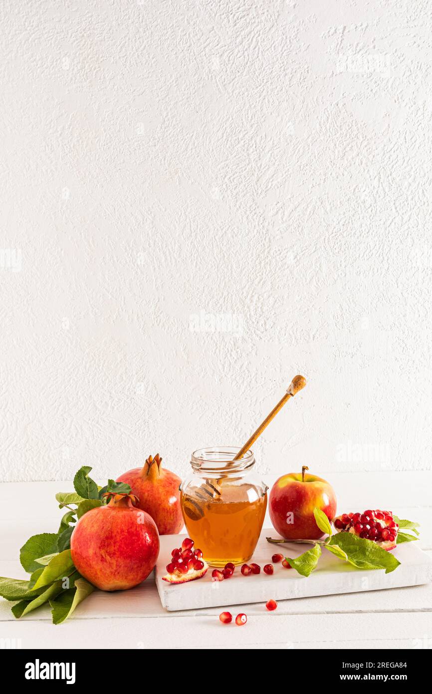 Bella natura morta con melograni maturi e mele, una ciotola di miele. Sfondo bianco. Il concetto di Rosh Hashanah. Uno spazio per le copie. Vista verticale Foto Stock