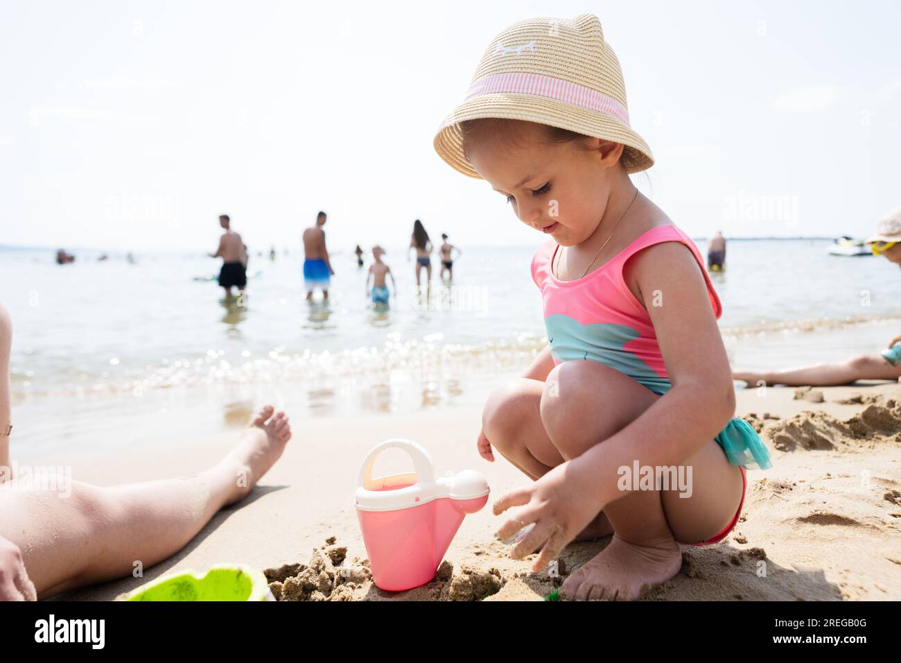 Una bambina carina che gioca con la sabbia sulla spiaggia durante il giorno d'estate. Foto Stock