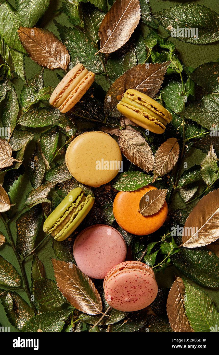 Macaron su uno sfondo verde e dorato con foglie viste dall'alto Foto Stock