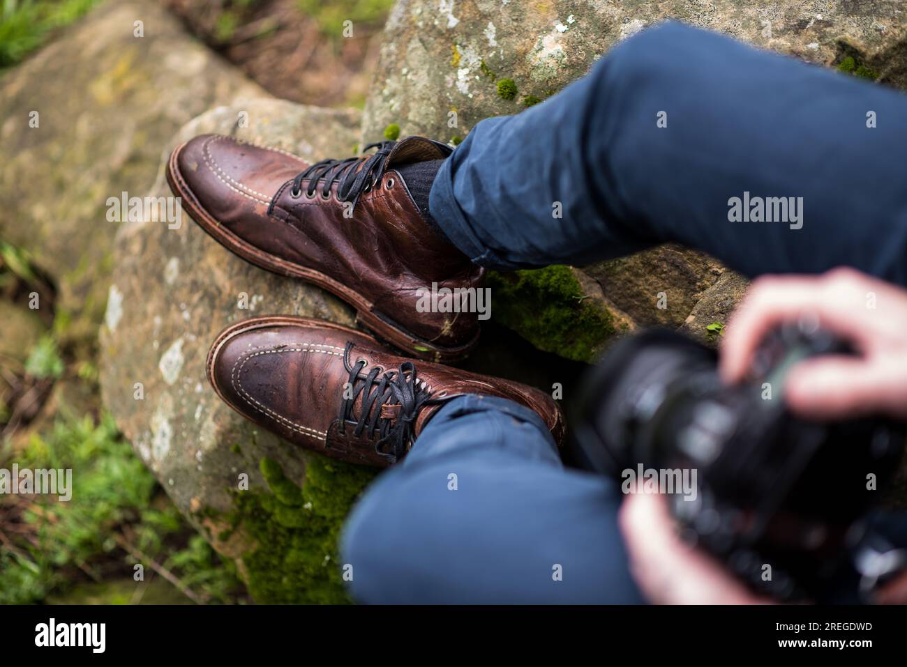 Uomo che indossa stivali di pelle seduti su rocce con la fotocamera Foto Stock