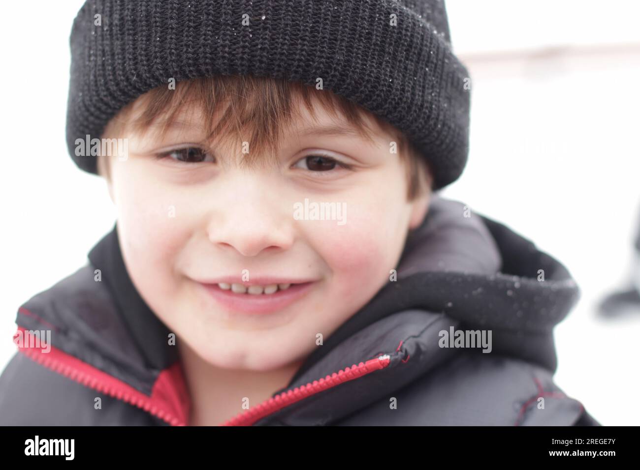 il bambino gioca nella neve con un berretto che mette in mostra il suo viso dolce Foto Stock