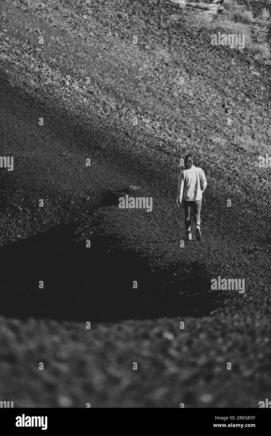 bianco e nero di una donna che si allontana su un sentiero di sabbia nera Foto Stock