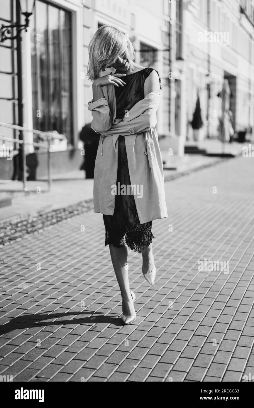 Bella donna bionda con un abito in pizzo su una strada cittadina, sorriso felice. Foto Stock