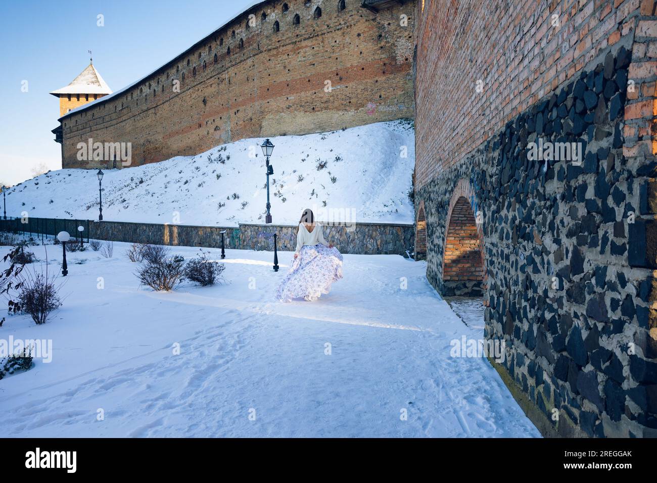 Una ragazza con un lungo abito cammina lungo le mura del castello al tramonto Foto Stock