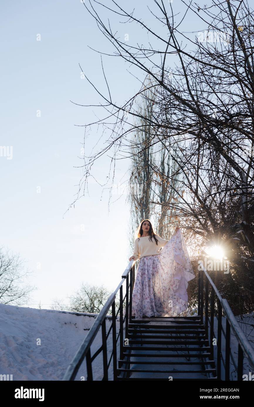 La ragazza scende le scale con un lungo vestito al tramonto Foto Stock
