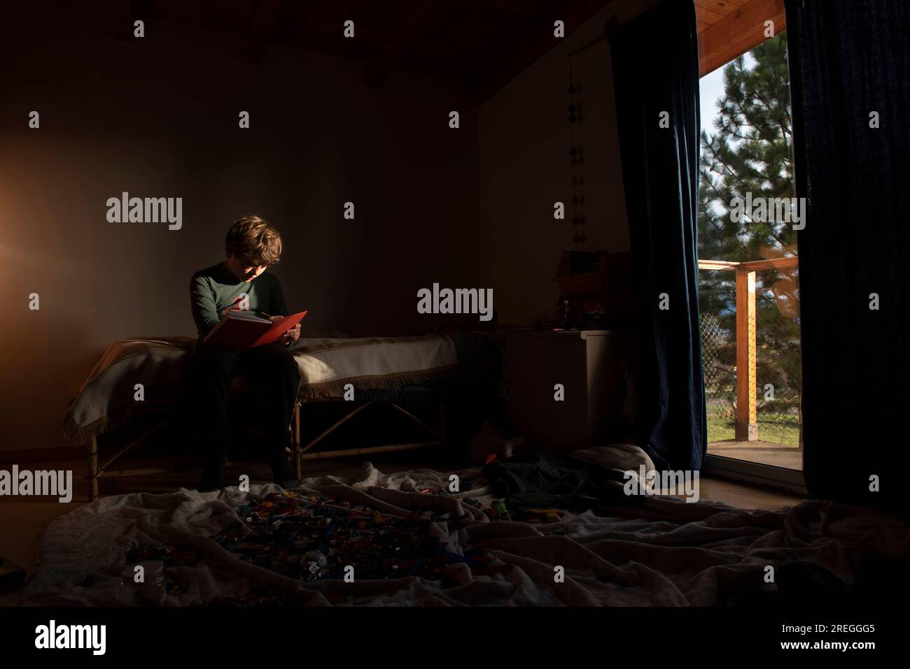 Un ragazzo seduto sul letto con un notebook in una stanza con leghi Foto Stock