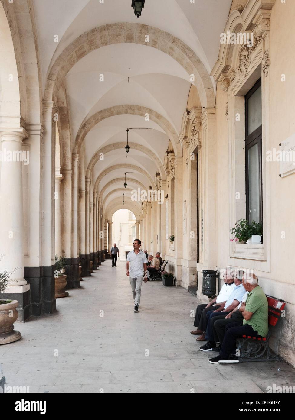 Anziani seduti su una panchina nel portico del Municipio di Palazzolo Acreide, Sicilia, Italia Foto Stock