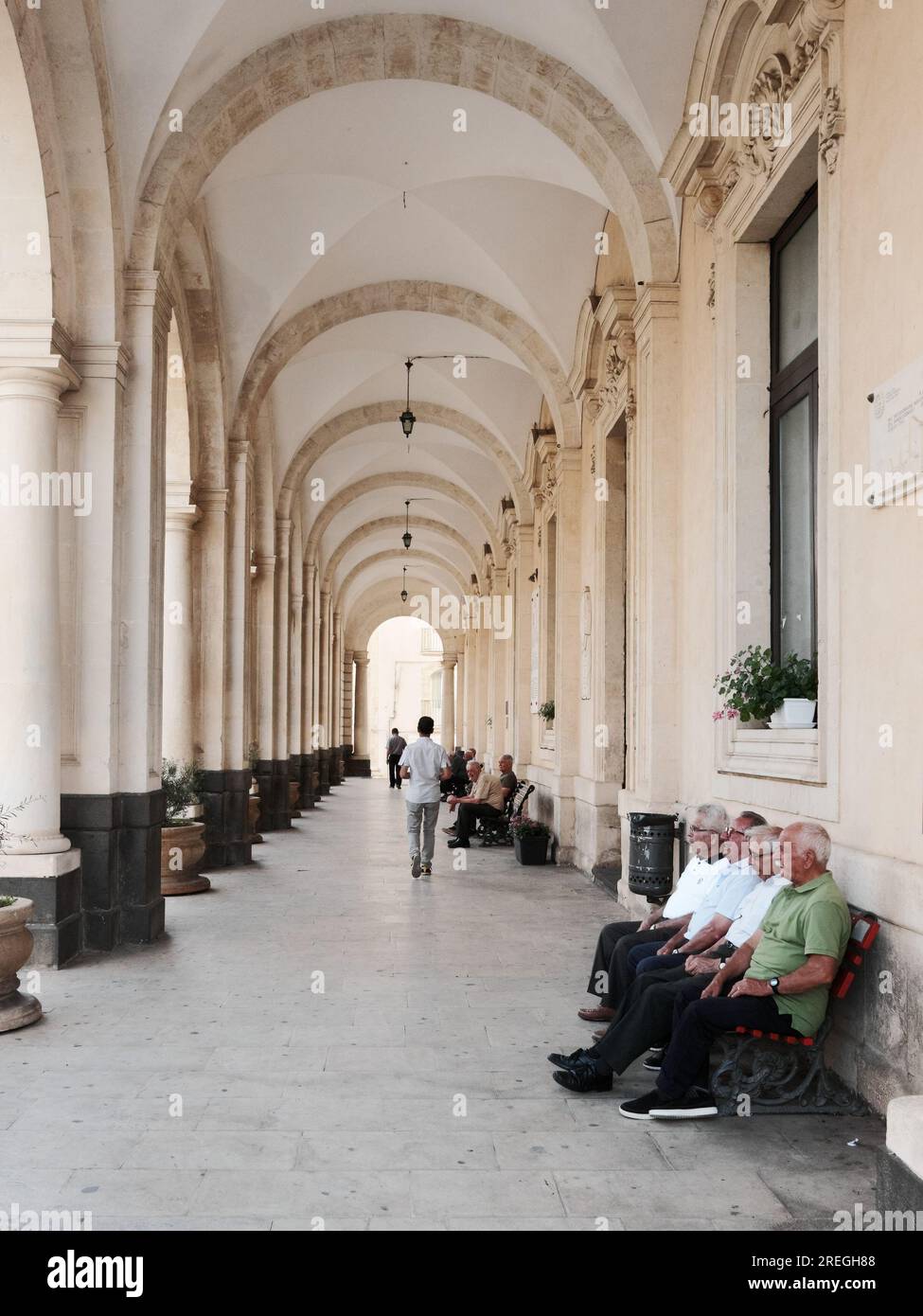 Anziani seduti su una panchina nel portico del Municipio di Palazzolo Acreide, Sicilia, Italia Foto Stock