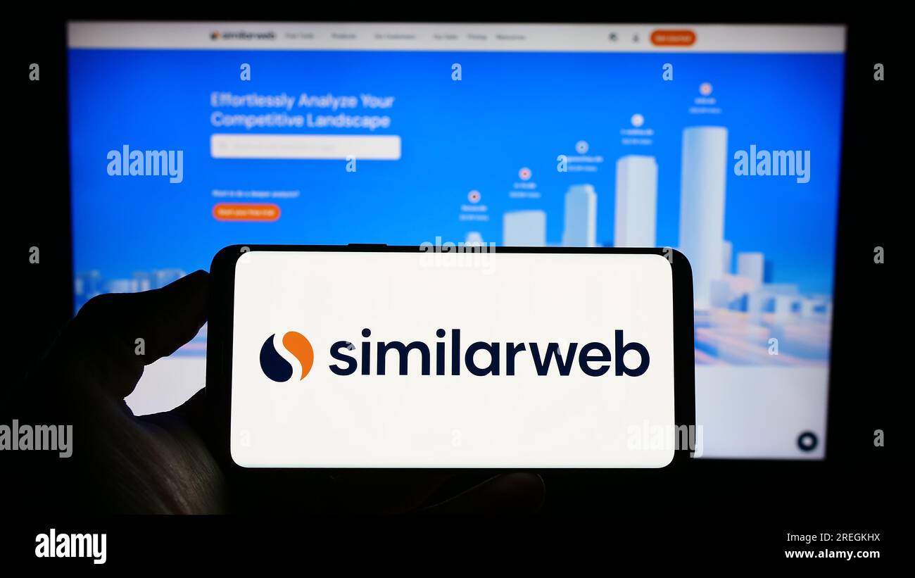 Persona in possesso di un cellulare con il logo della società israeliana di analisi web SimilarWeb Ltd. Sullo schermo davanti alla pagina Web. Concentrarsi sul display del telefono. Foto Stock