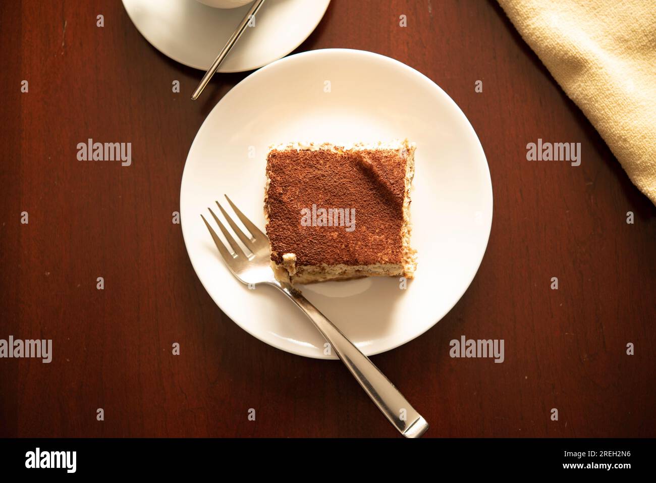 Fetta di tiramisù tradizionale italiano su piatto bianco e tavolo in legno con forchetta e tazza di caffè. Foto Stock