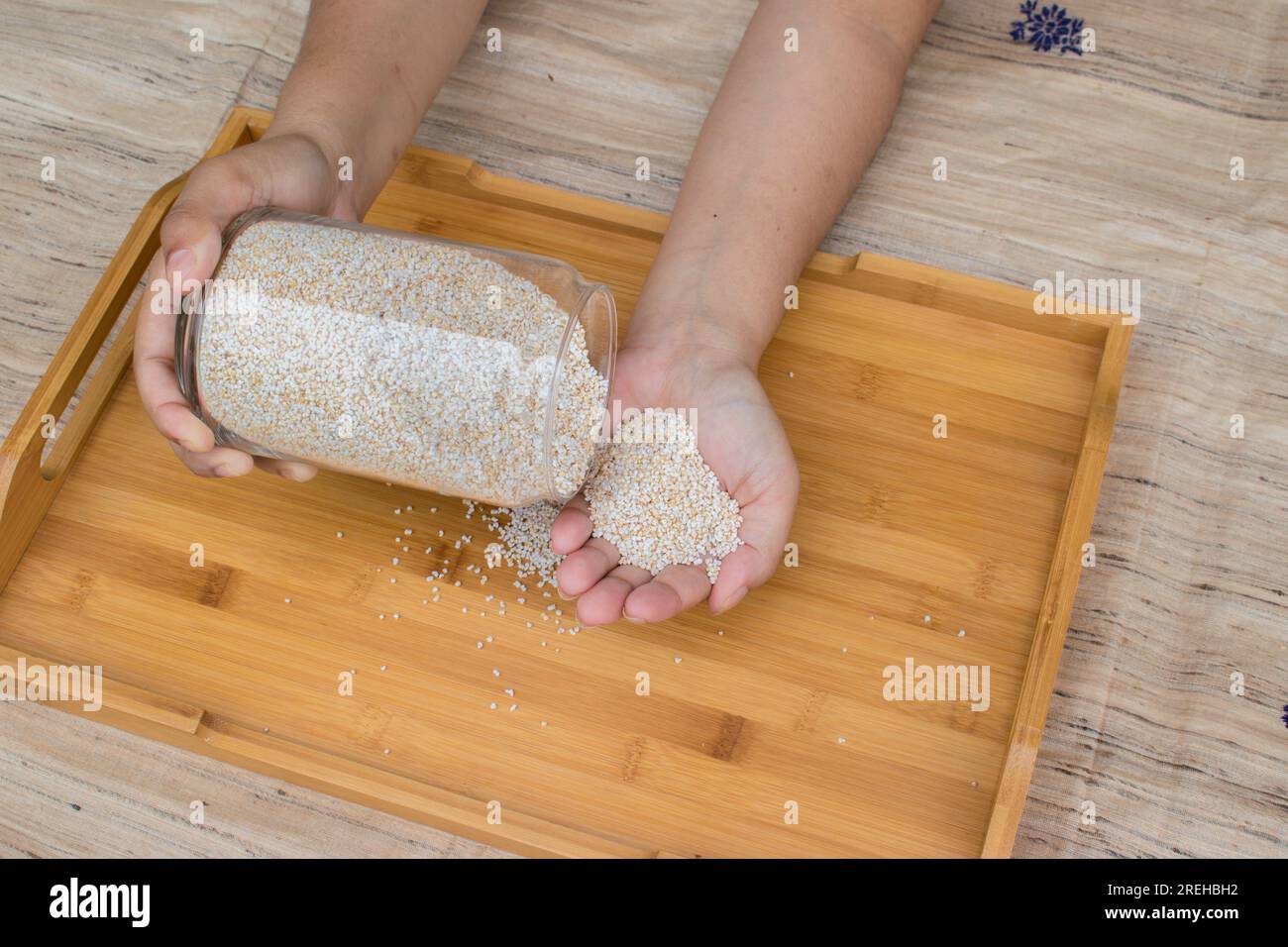 Porta a mano un vaso di vetro contenente amaranto o ramdana o rajgira gonfiato su un vassoio di legno È un chicco senza glutine che fornisce fibre e proteine Foto Stock