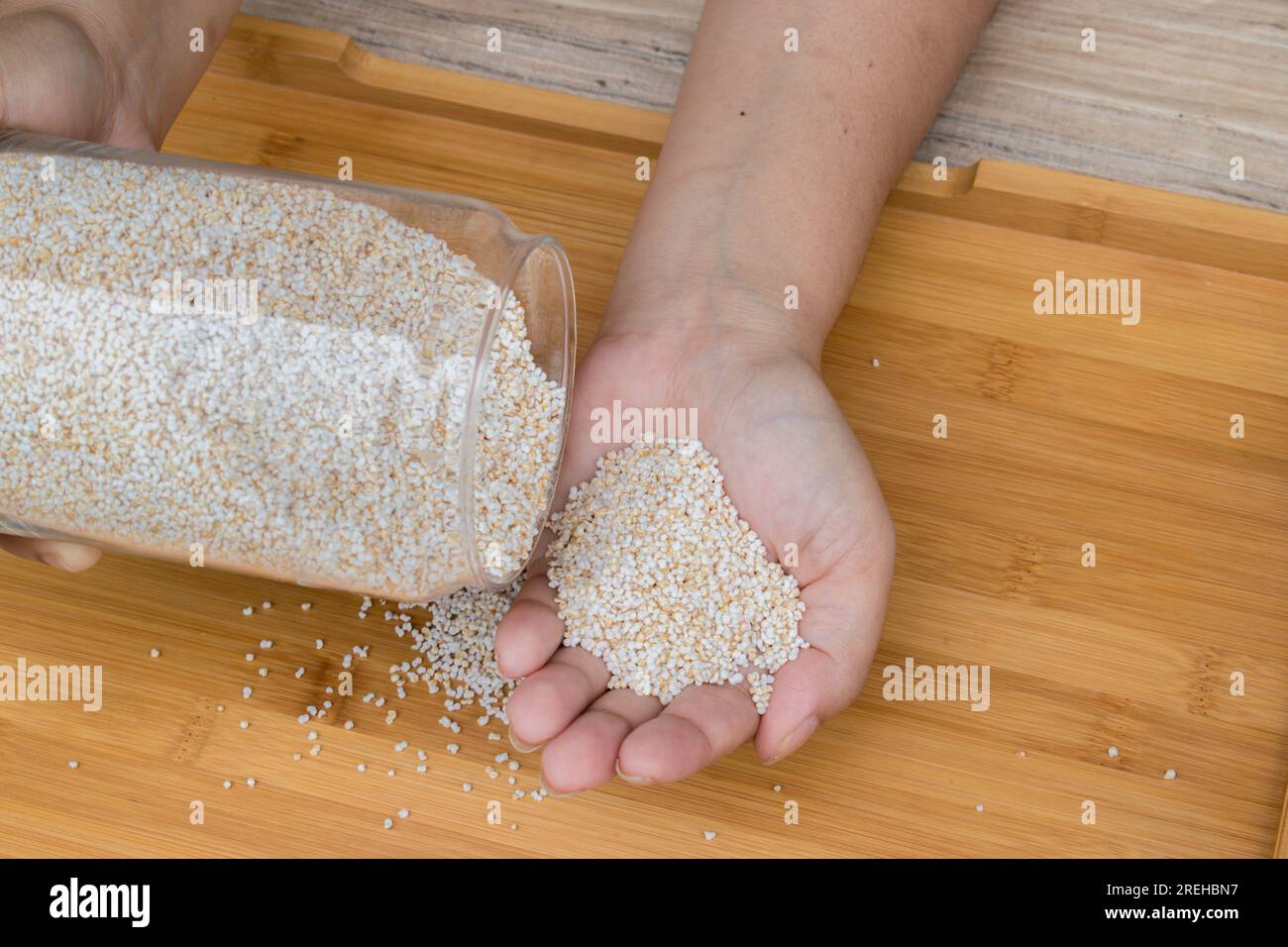 Porta a mano un vaso di vetro contenente amaranto o ramdana o rajgira gonfiato su un vassoio di legno Si tratta di un chicco senza glutine che fornisce fibre Foto Stock