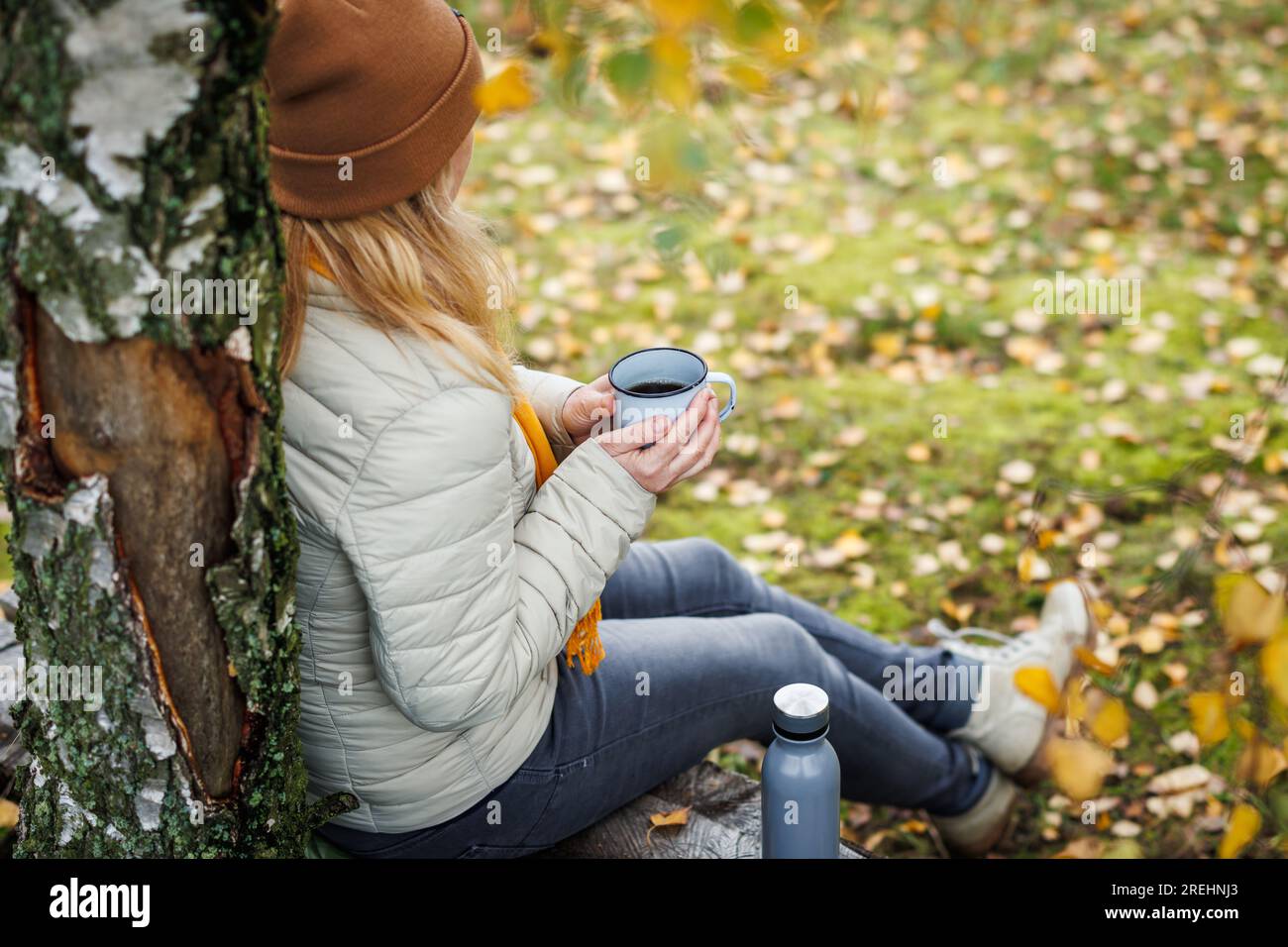 Donna che beve bevande calde e riposa sulla panchina nella foresta. Relax durante le escursioni autunnali Foto Stock